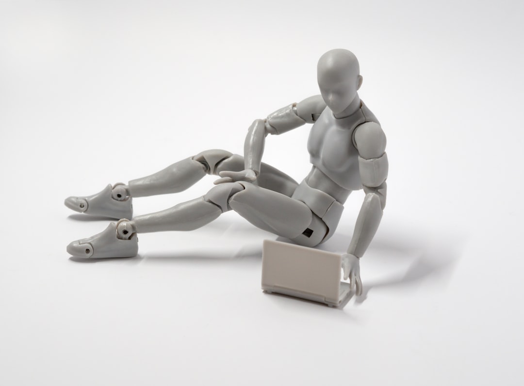 grey man action figure sitting on floor with laptop