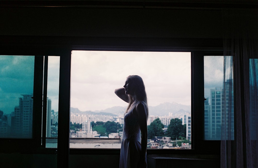 a woman standing in front of a window looking out at a city