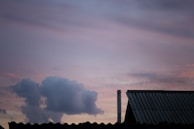 A quiet outdoor scene with a chimney smoke curling into a pastel sunset sky.