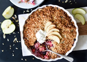 Close-up of a rustic apple crumble with golden, crumbly topping in an earth-toned ceramic dish.