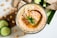 Close-up of smooth, creamy hummus topped with toasted pine nuts and fresh herbs.
