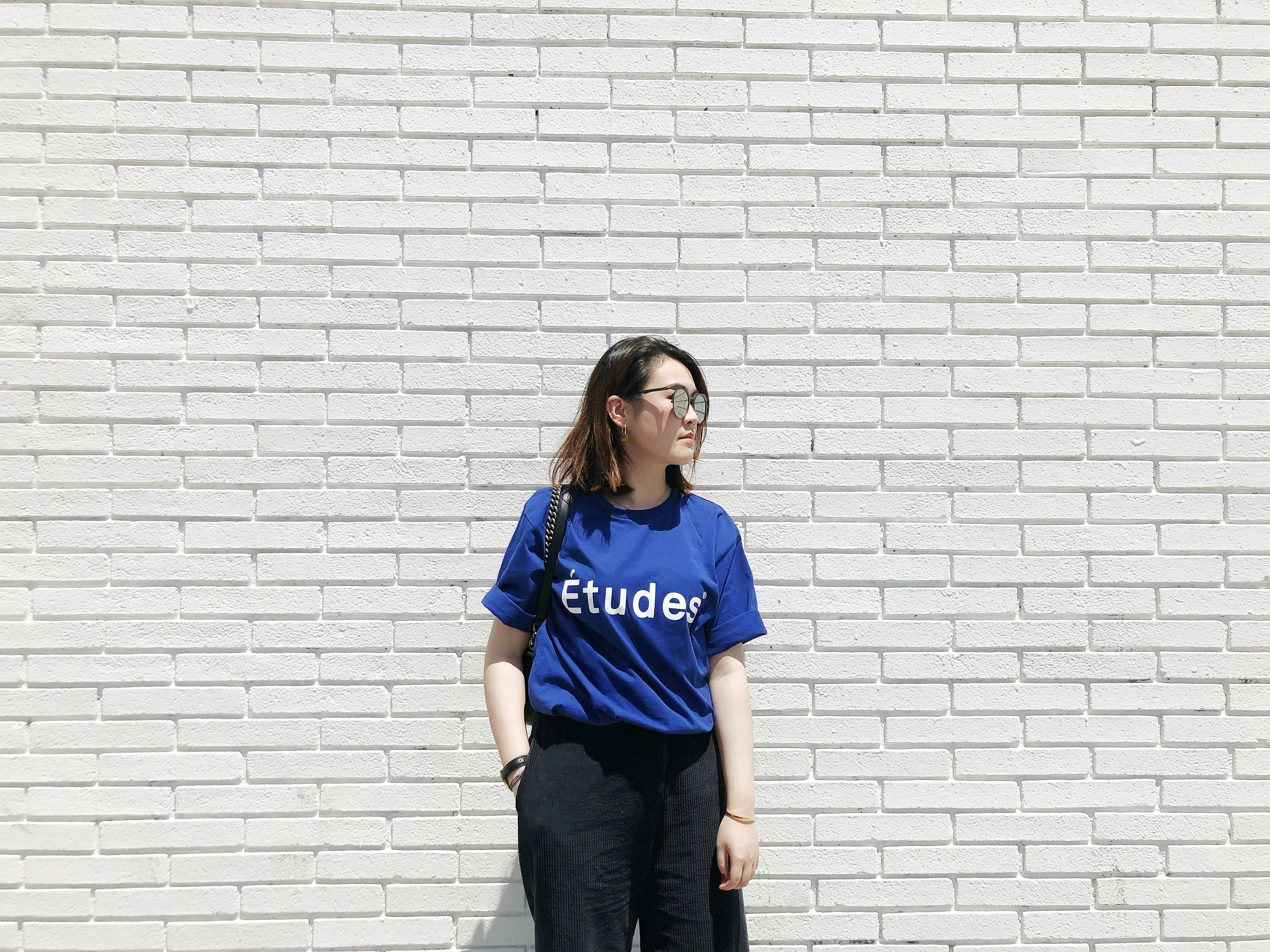 woman blue Etudes shirt standing by white brick wall