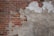 A wall with peeling plaster revealing red bricks beneath. The plaster is mostly worn away on the left side, exposing more of the textured brick surface. The remaining plaster is discolored and weathered, giving a rugged appearance.