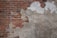 A wall with peeling plaster revealing red bricks beneath. The plaster is mostly worn away on the left side, exposing more of the textured brick surface. The remaining plaster is discolored and weathered, giving a rugged appearance.