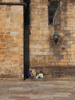 two people sitting at the side of the building