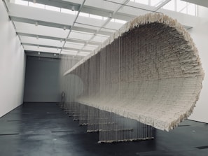 A large mixed-media wall installation with layered textures and earthy tones in a softly lit gallery space