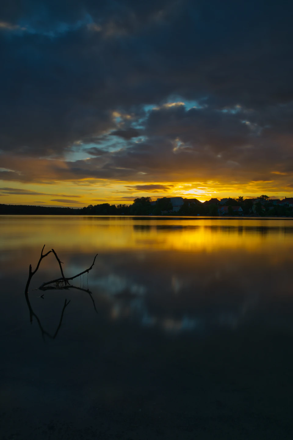 Serene lake at sunset with orange and blue hues, sun sets behind horizon slowly