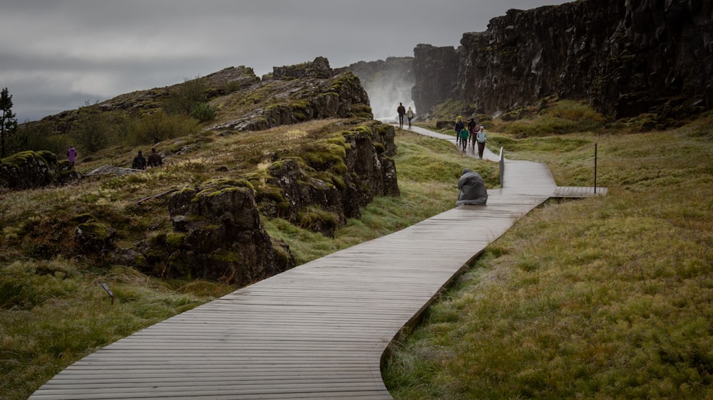 people walking wooden footbridge towards the waterfall