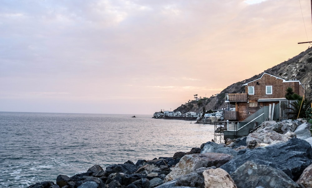brown wooden house on rocky shore under grey cloudy sky