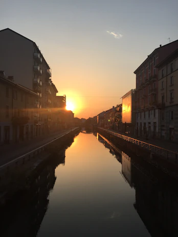 Sunset over the canal with silhouettes of boats and mangroves, casting warm orange and green hues.