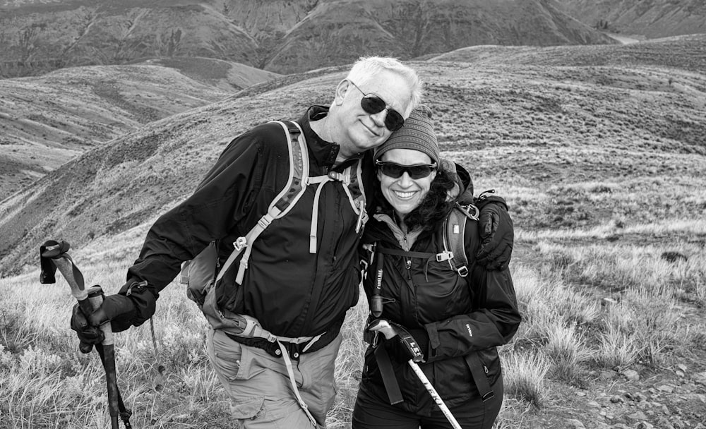 grayscale photography of man and woman standing near mountain