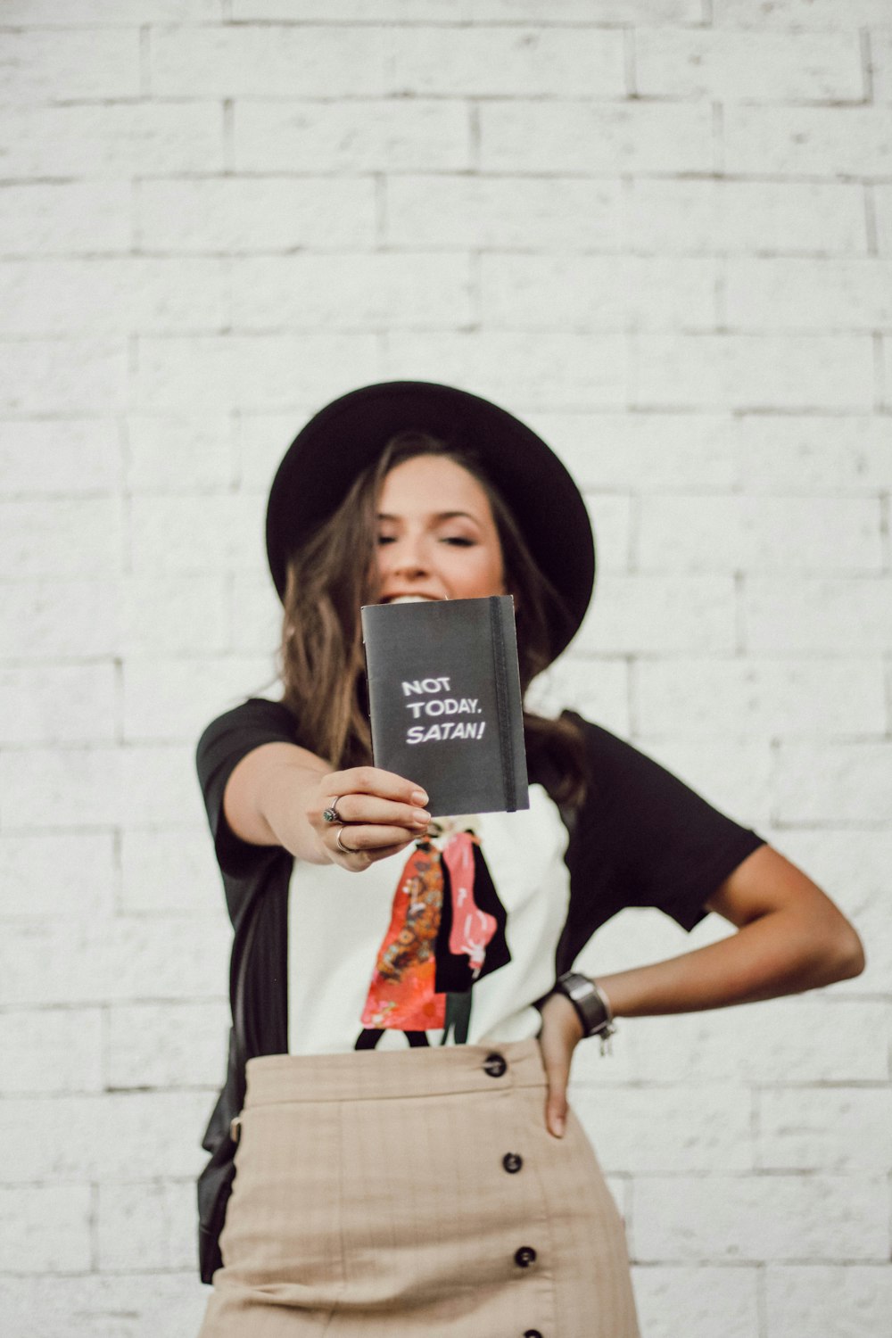 woman with left arm akimbo standing and smiling while holding booklet