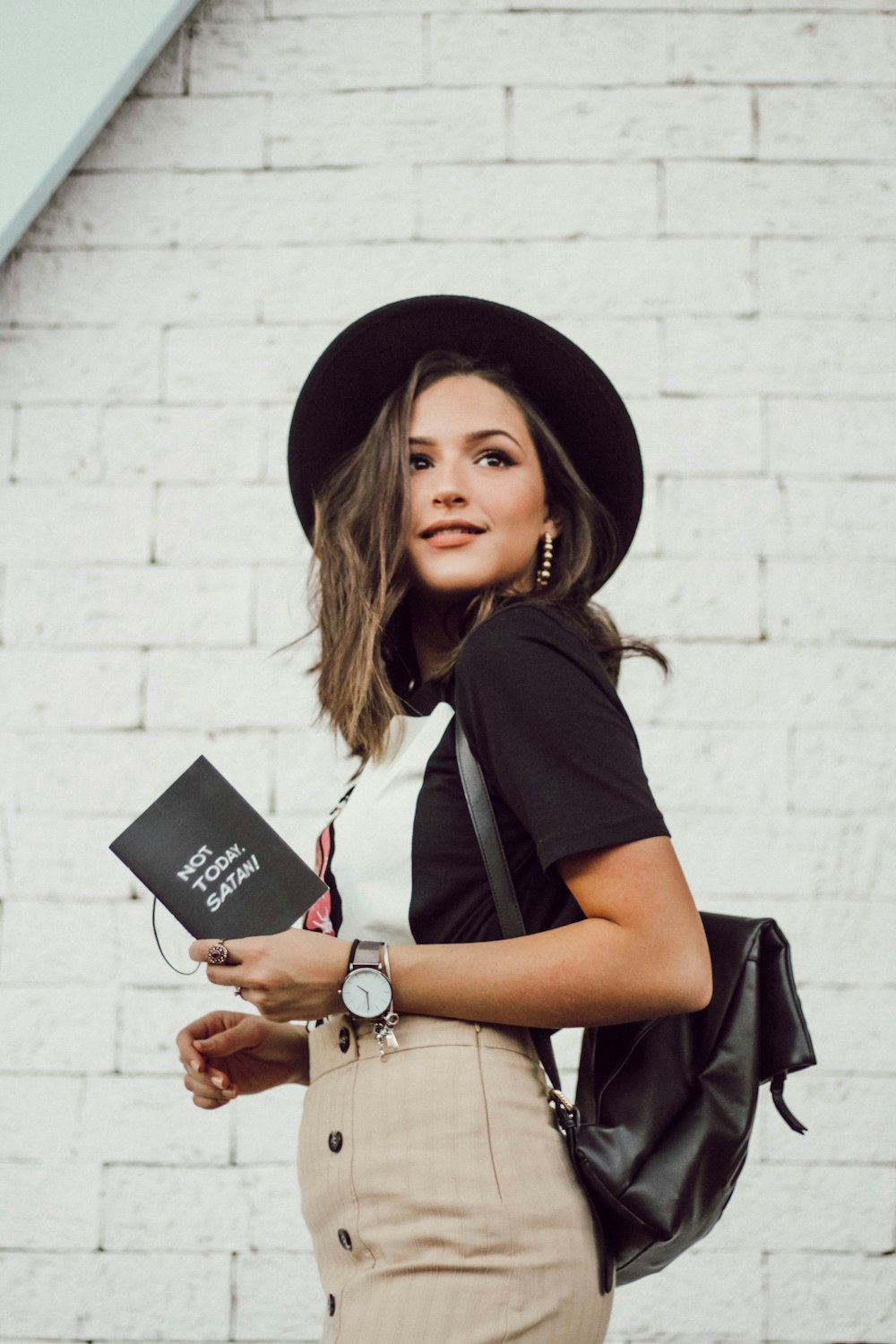 woman in black blazer and brown dress holding booklet while looking into left side and smiling