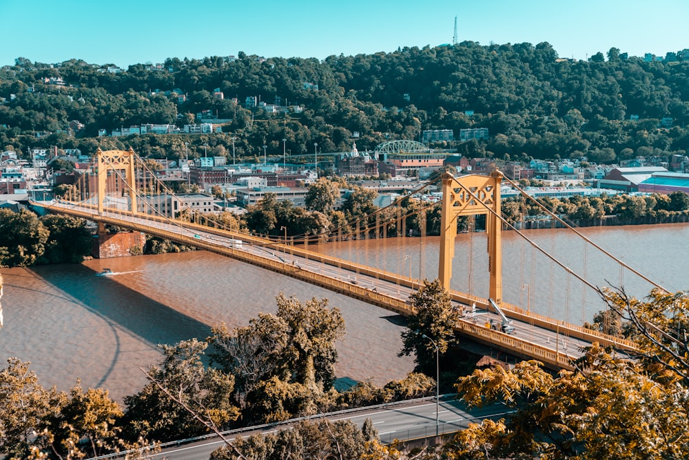 vehicles passing suspension bridge across the river during daytime