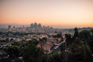 A warm, inviting modern home exterior with a city skyline in the background at sunset.