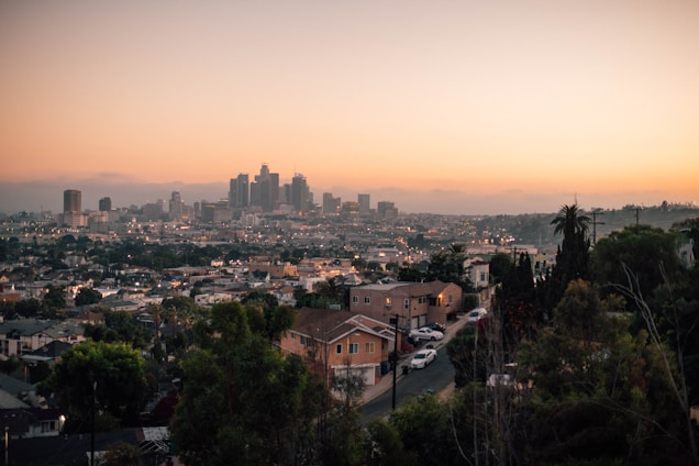 A warm, inviting modern home exterior with a city skyline in the background at sunset.