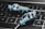 Two blue in-ear headphones with cables rest on a laptop keyboard. The keyboard keys are backlit in white, and the headphones have a sleek design with a prominent logo on the earpiece.