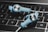 Two blue in-ear headphones with cables rest on a laptop keyboard. The keyboard keys are backlit in white, and the headphones have a sleek design with a prominent logo on the earpiece.