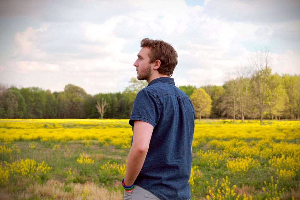 homme en polo bleu et pantalon gris debout dans un champ de fleurs jaunes