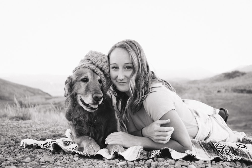 grayscale photography of smiling girl lying on textile beside golden retriever