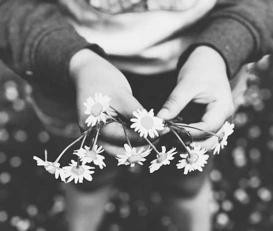 A serene black-and-white portrait of a child holding a small bouquet of wildflowers.
