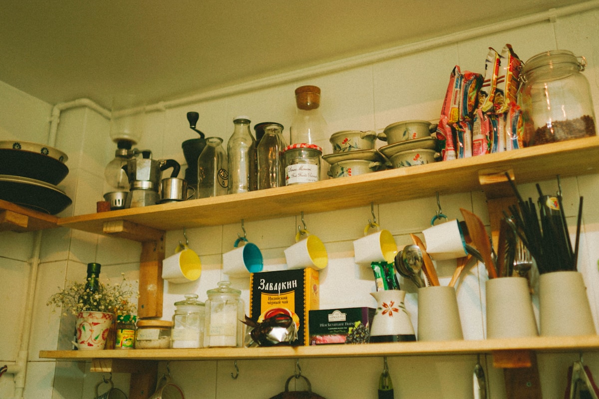 Real apartment kitchen with high-mounted wooden shelves and hanging cup hooks above cabinets