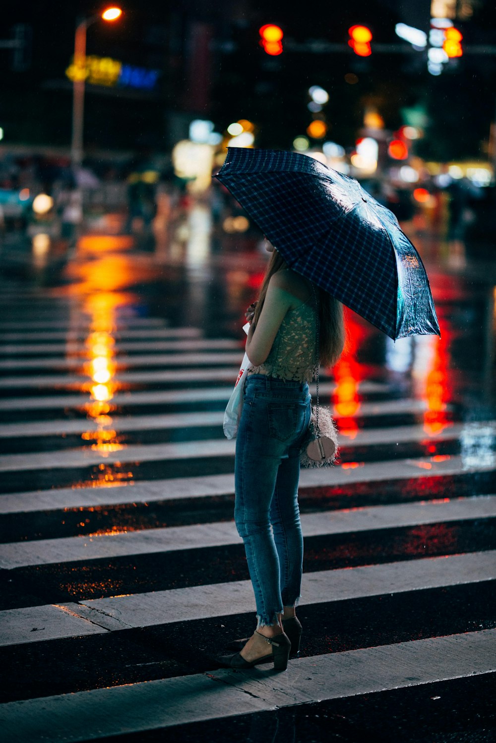 Mujer en jeans azules de pie en el carril peatonal sosteniendo un paraguas
