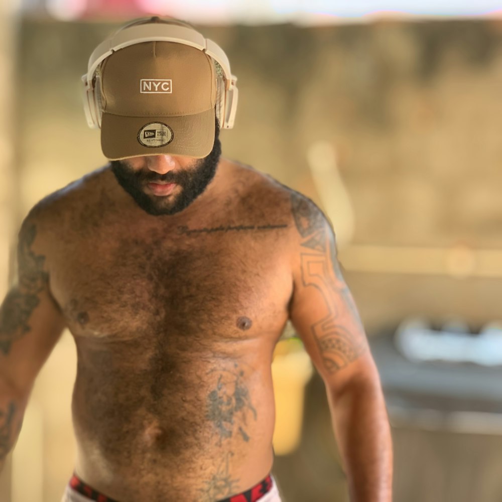 topless man wearing brown NYC cap and headphones