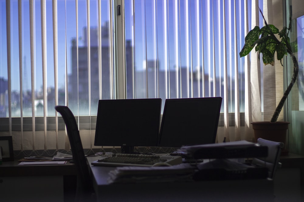 two black flat screen monitors on desk near window