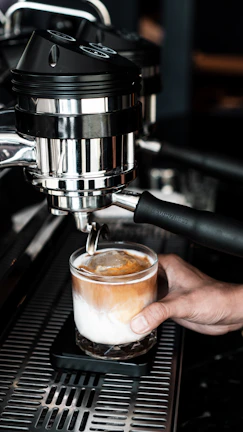 Barista carefully pouring espresso into a glass, capturing the smooth crema on top.