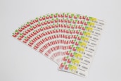 A collection of labels arranged in a fanned-out pattern, each featuring illustrations of a red factory with a green chimney and a yellow area with text and barcodes. The labels are neatly organized on a white background.