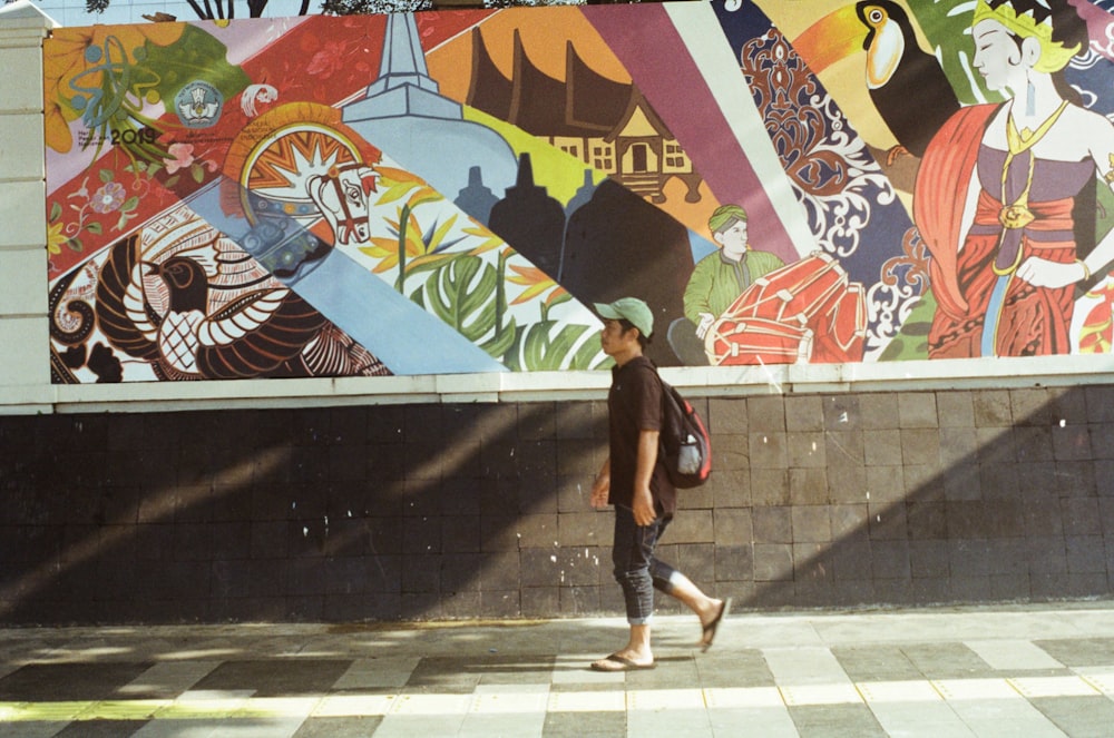 man in brown short-sleeved walking on street passing painting