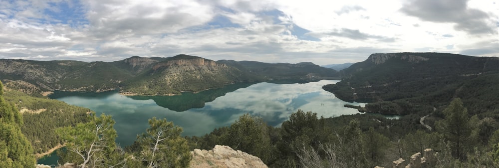 a lake surrounded by mountains and trees under a cloudy sky