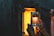 Hands holding a smartphone capturing an image of a glowing orange furnace or kiln. The scene is set in a dimly lit industrial environment, with the light from the furnace contrasting with the dark surroundings.
