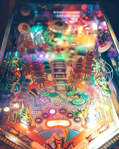 A colorful pinball machine with a vibrant, intricate design featuring various lights and artwork. The playfield includes numerous bumpers, targets, and ramps that contribute to a lively and dynamic game experience.