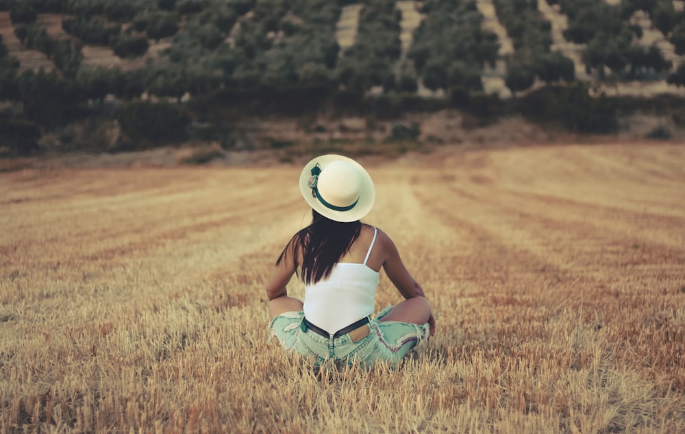 woman wearing white sunhat sitting on brown grassland during daytime