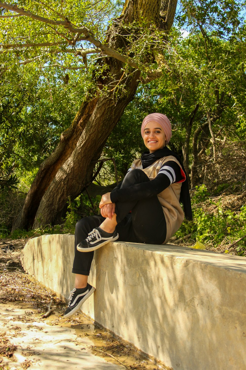 women sitting in a concrete wall under tree during daytime