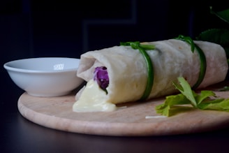 Close-up of a falafel wrap with fresh vegetables and tahini sauce on a rustic wooden board.