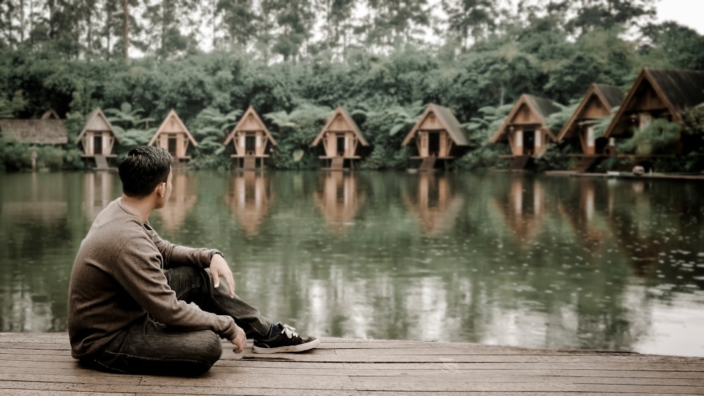 man sitting on dock near lake
