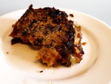 A slice of rich date and walnut cake on a simple white plate with a fork beside it.