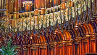 An ornate section of a building featuring intricate wooden carvings and gilded decorations. The design includes geometric and floral patterns, highlighted by ambient lighting. The architecture is Gothic-inspired with pointed arches and richly detailed moldings.