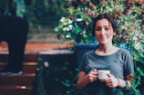 Smiling person enjoying a peaceful moment with a cup of herbal tea surrounded by plants.
