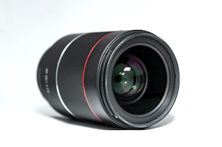A sleek black and white close-up of a vintage film camera lens with subtle red accents.