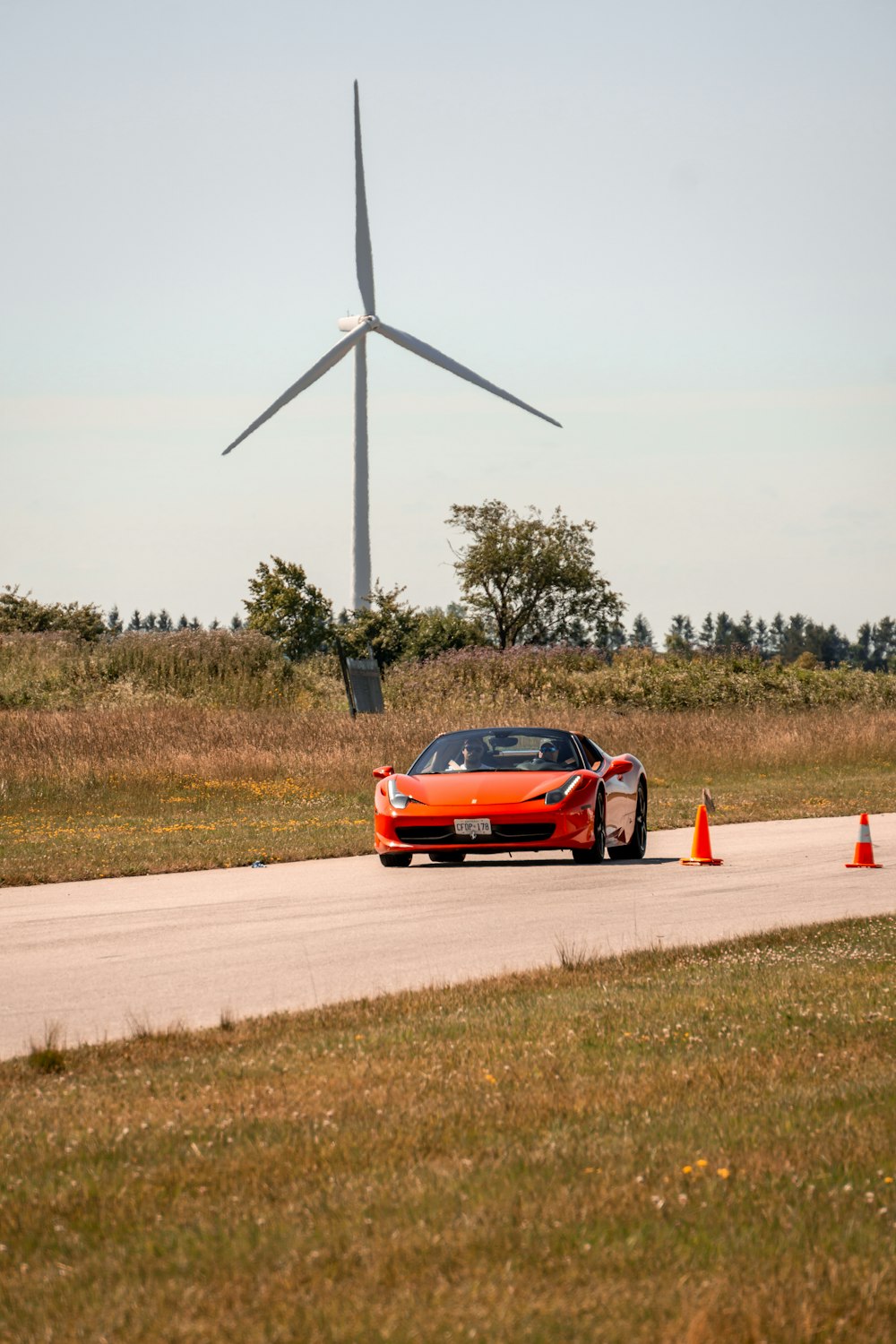 orange Ferrari 458 coupe traveling on road near turbine