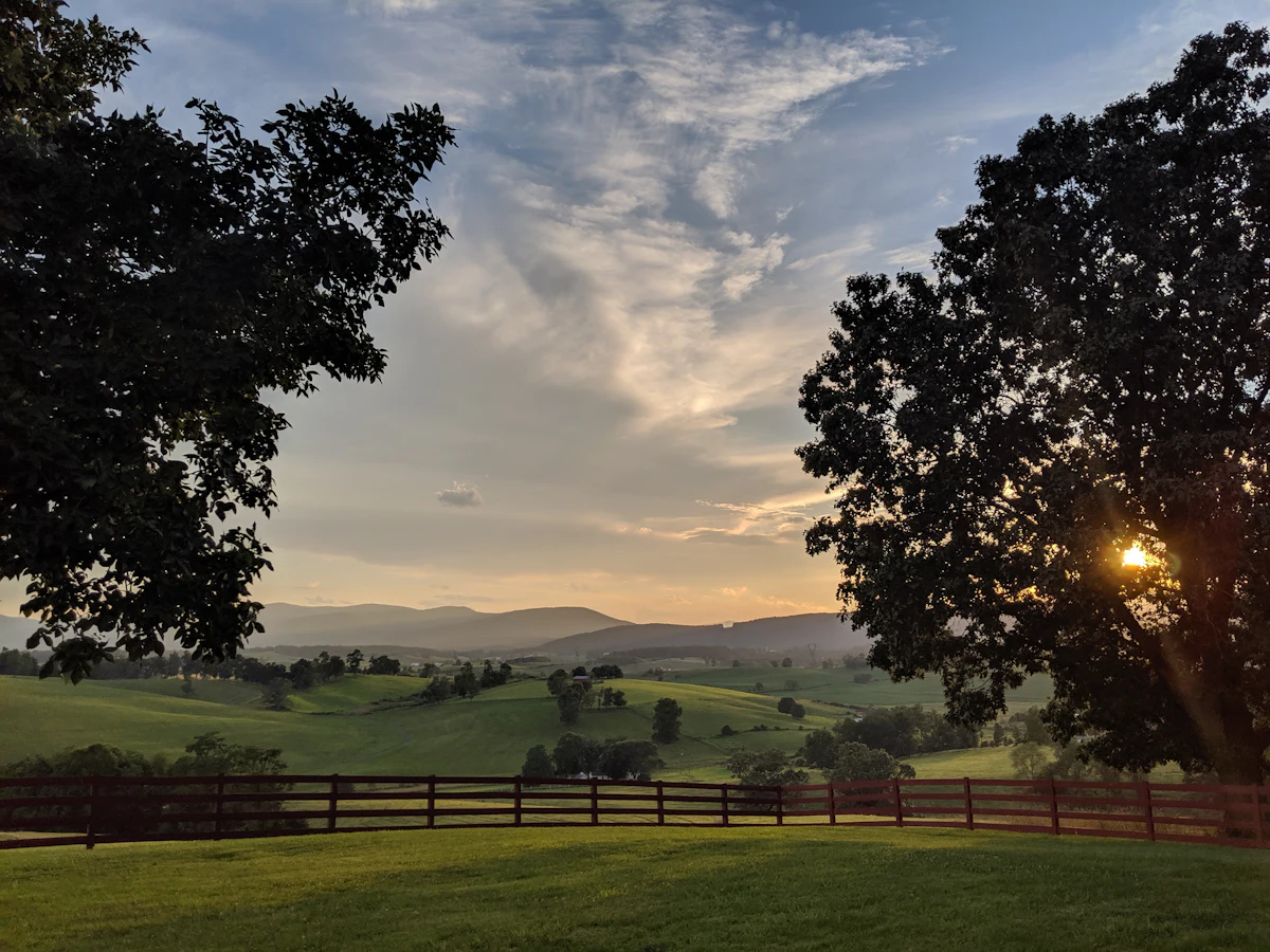 A fenced pasture near Churchville, Virginia at sunset, with low mountains behind and big trees either side