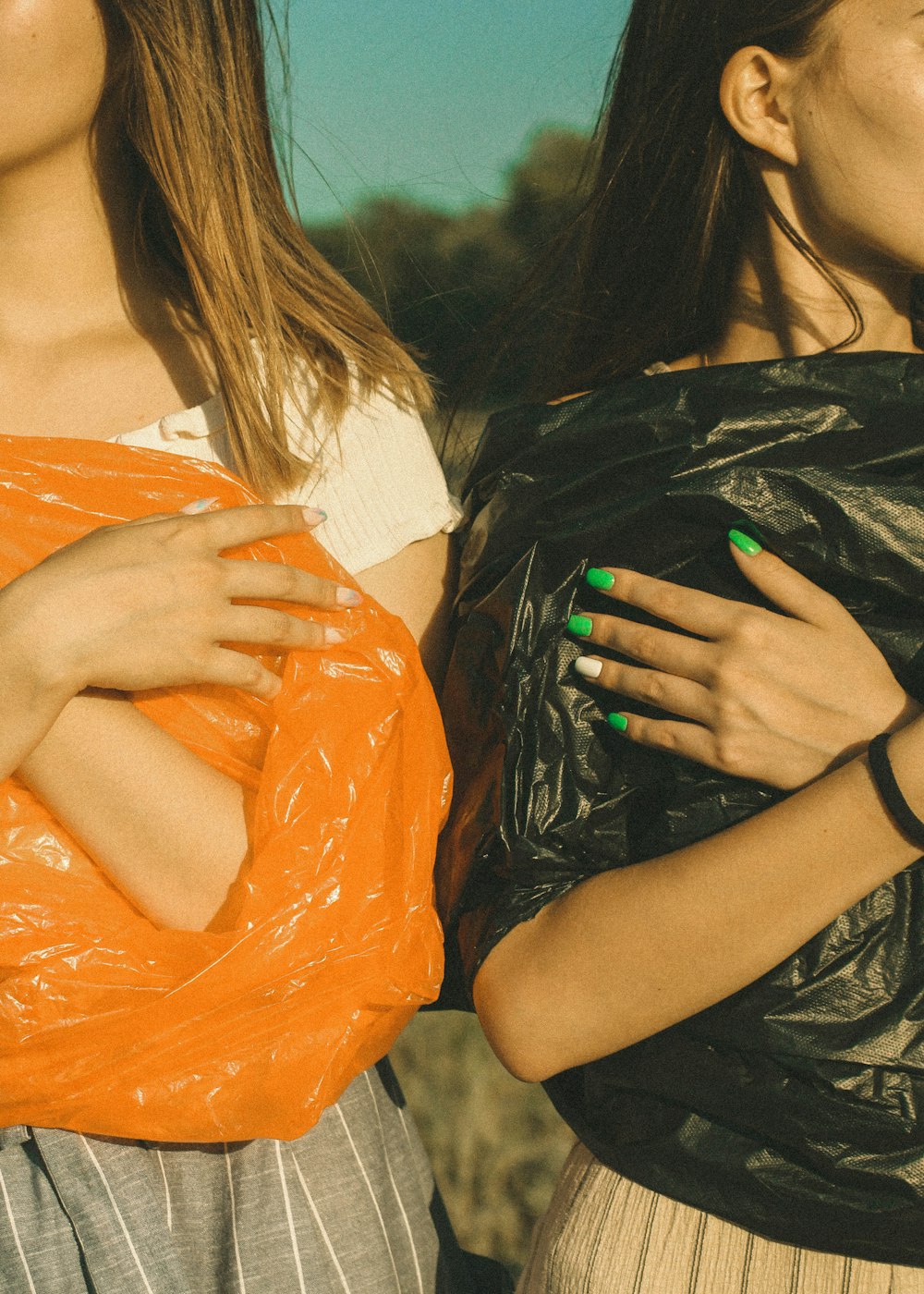 duas mulheres vestindo sacos plásticos pretos e laranjas
