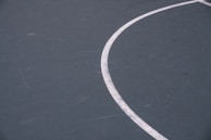 A close-up view of a section of a sports court features a curved white line on a dark green surface. The texture of the court is visible with some minor scuffs and marks.