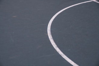 A close-up view of a section of a sports court features a curved white line on a dark green surface. The texture of the court is visible with some minor scuffs and marks.