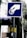 A blue and white sign depicts a hand inserting a coin into a slot or meter. The background includes a building, trees, and a utility pole with wires.