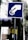 A blue and white sign depicts a hand inserting a coin into a slot or meter. The background includes a building, trees, and a utility pole with wires.